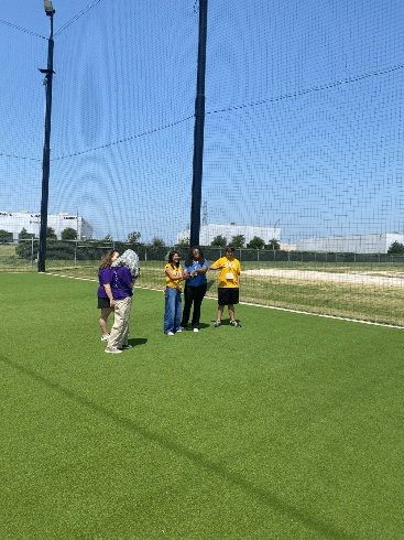 A group of students stand on an athletics field and talk to an instructor