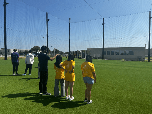 A group of students stand on an athletic field talking to an instructor