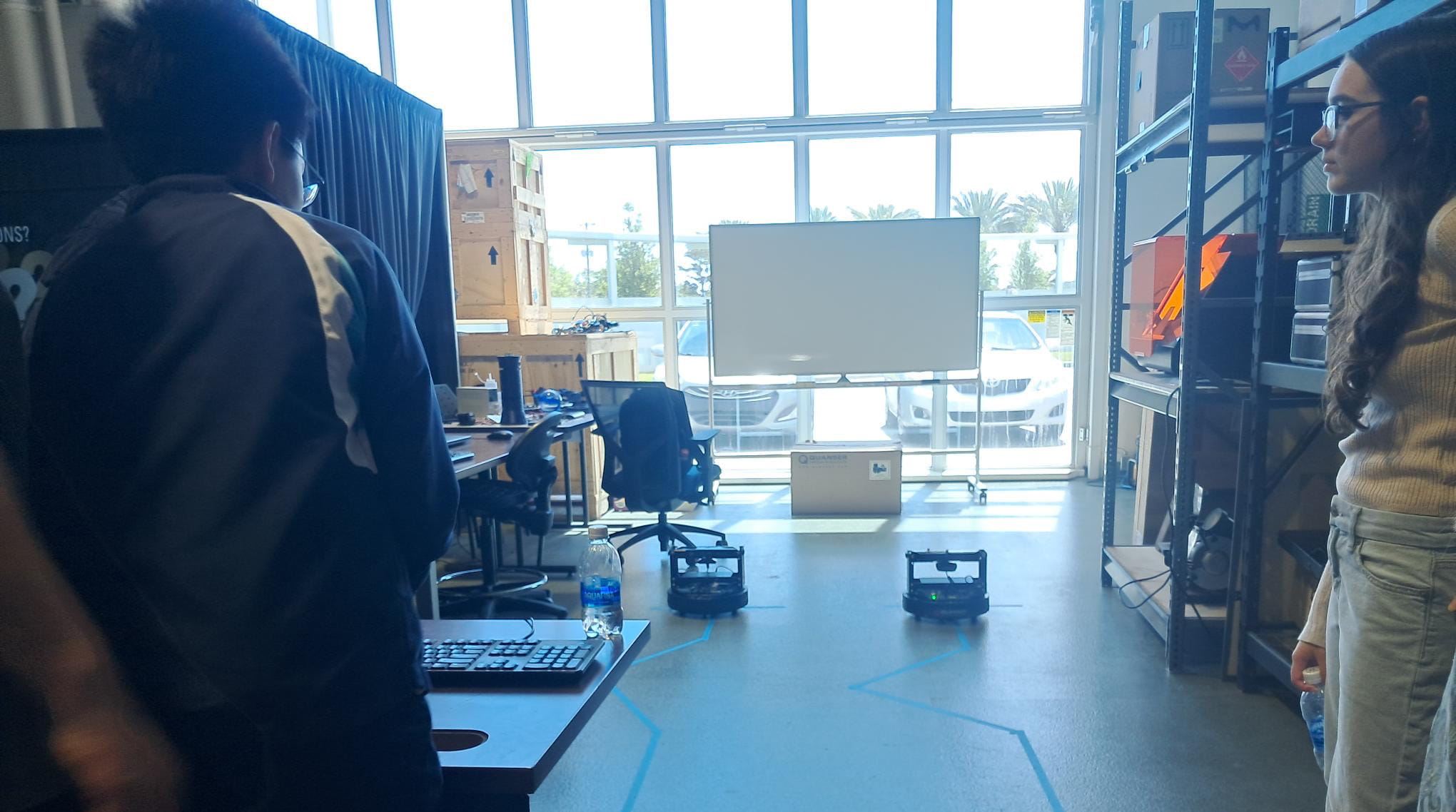 Students watch a couple of small unmanned vehicles in a lab.