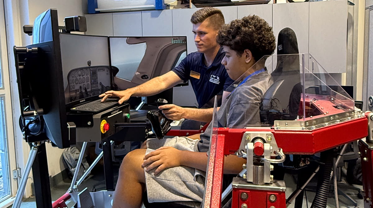Grade school student sits in a simulator for a plane.