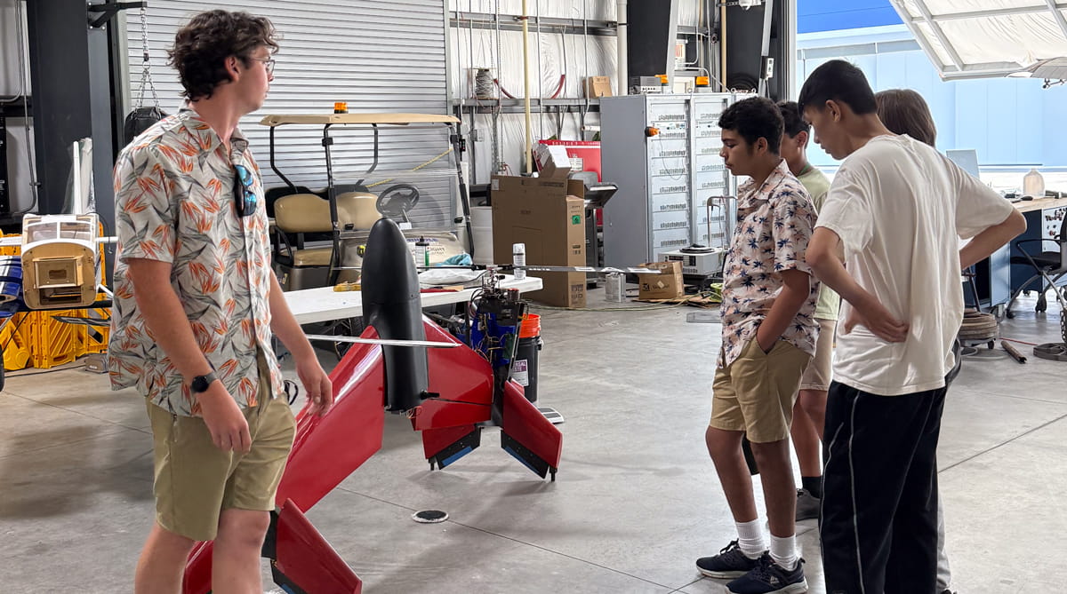 Students look at an unmanned aerial vehicle in a hangar