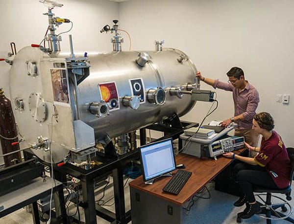 Two student researchers working with a plasma chamber