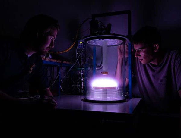 Two students surround the Pyrex glass chamber