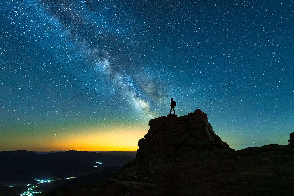 A man stands on a rock with the sun setting behind him