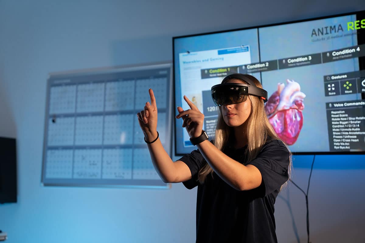A person wearing a VR headset gestures in front of a screen.
