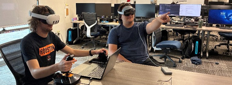 Two Embry-Riddle students sit at a table wearing VR headsets in the lab