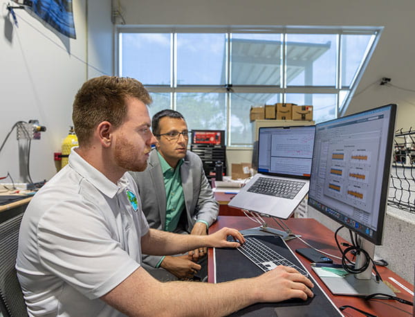 Professor of Aerospace Engineering Riccardo Bevilacqua and student Ryan Kinzi work together on computer in the ADAMUS Lab.