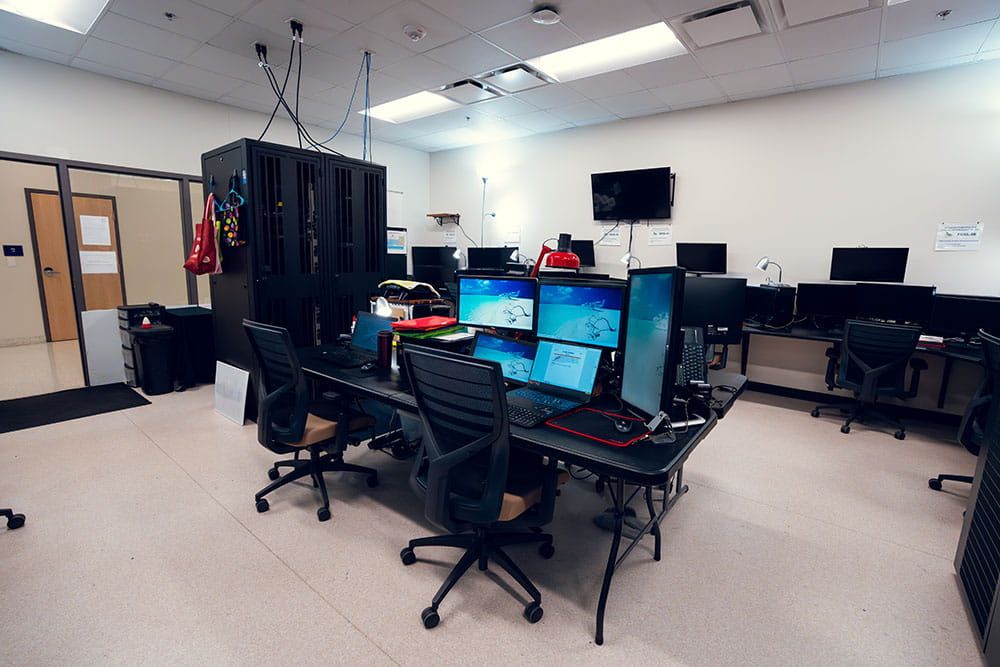 A lab with multiple computers, a TV screen and a server stack.