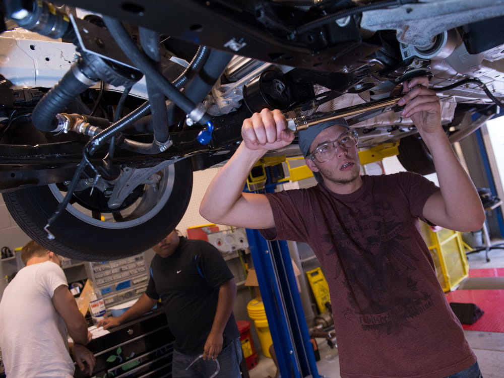 Student works on a car on a lift.