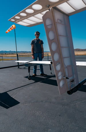 A person standing beneath an airplane wing on the tarmac.