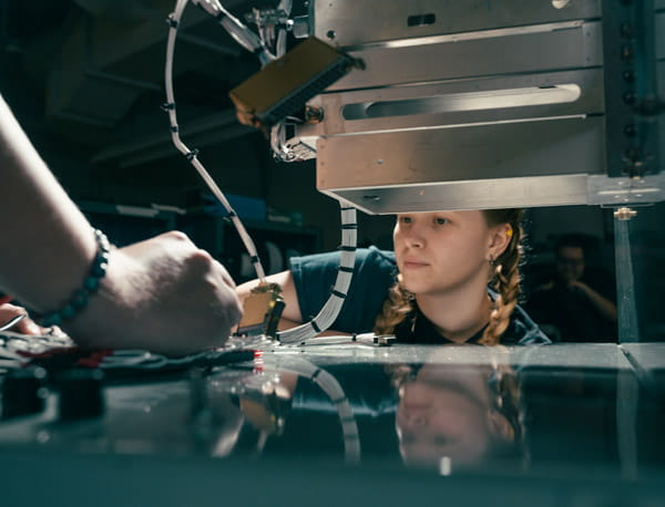 A person observing a machine as another person adjusts components.