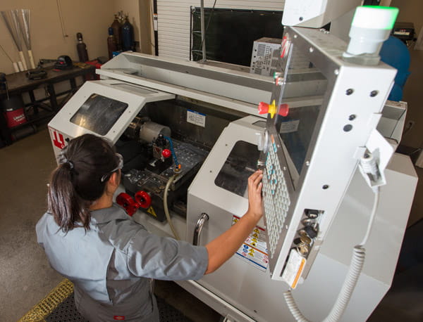 A person wearing safety glasses operating a CNC machine at an industrial workstation.