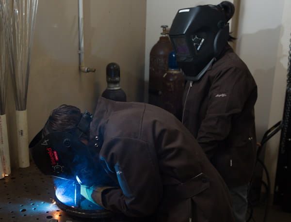Two people wearing safety equipment, welding some equipment.