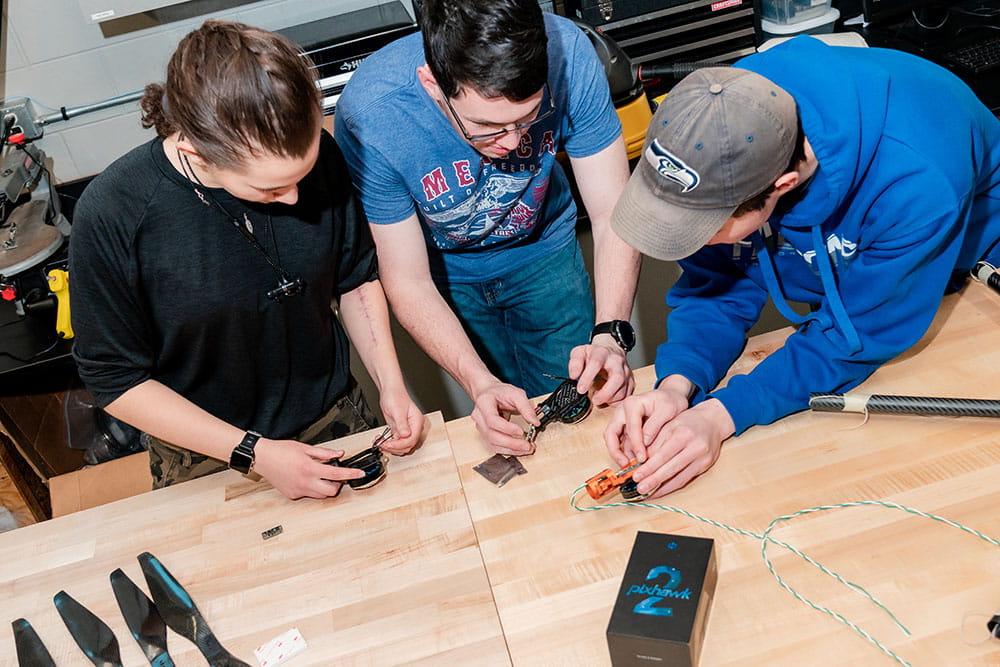 Three individuals working on flight controller equipment in a laboratory setting