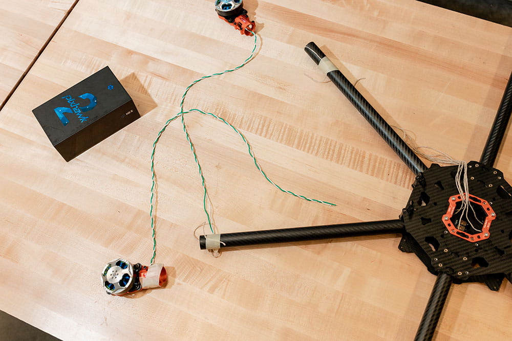 A tabletop workspace with a flight controller sitting on a wooden surface