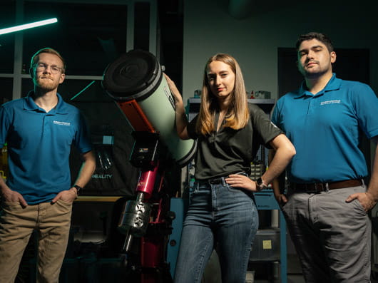 Three people standing next to a large telescope.