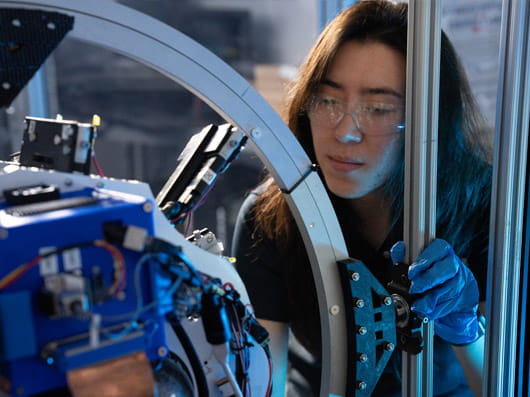 A person wearing safety googles, looking at equipment in a laboratory.