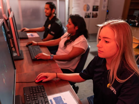 Three people seated side by side, each using a laptop or computer.