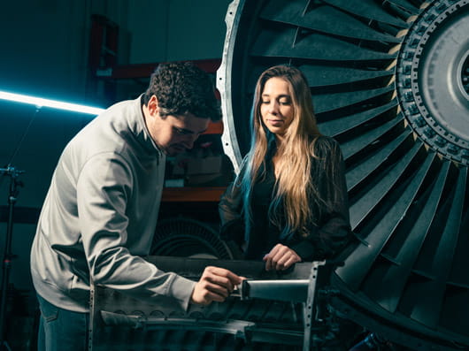 Two people working together with a large turbine in the background.