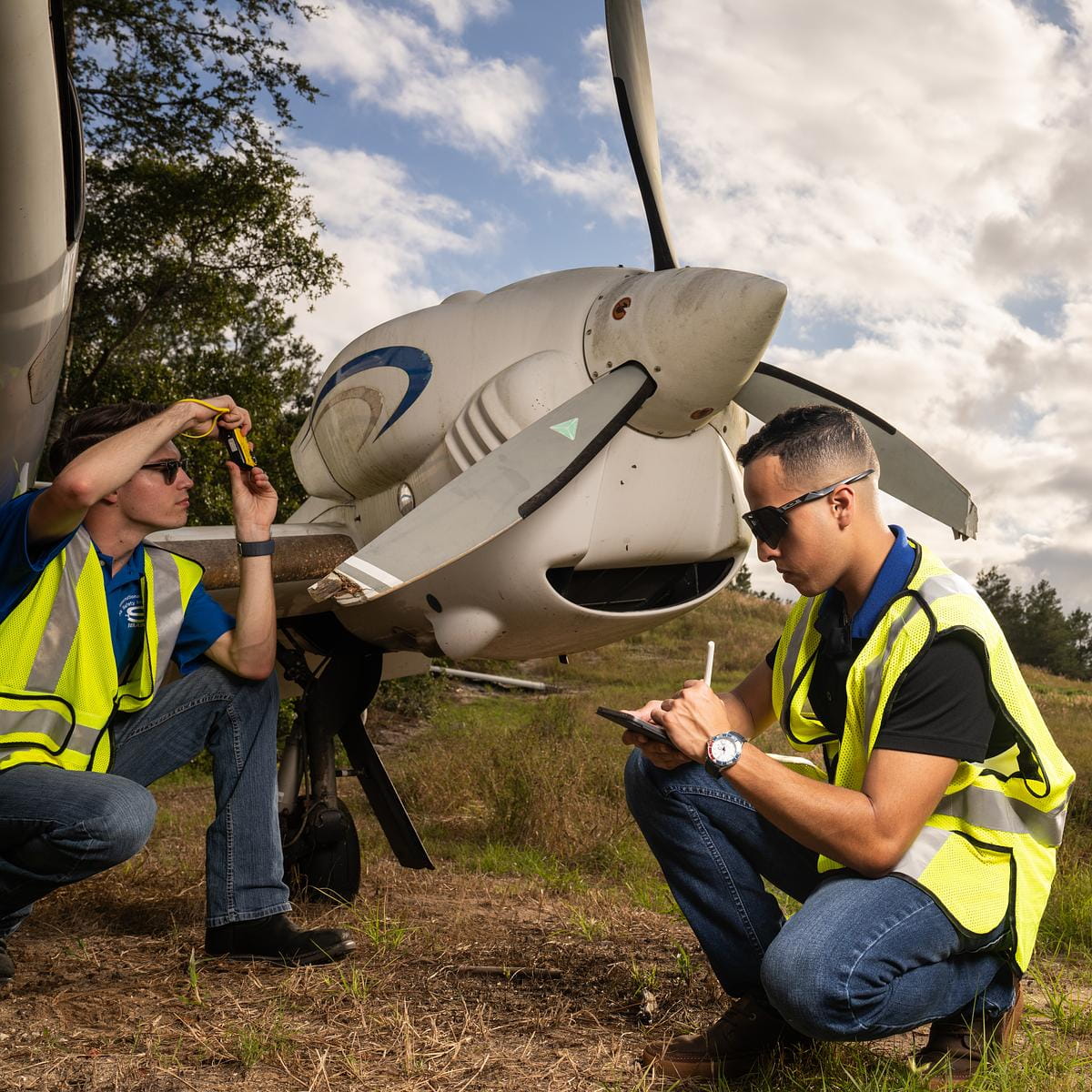 Embry-Riddle students in safety vests examine a plane propeller in a field