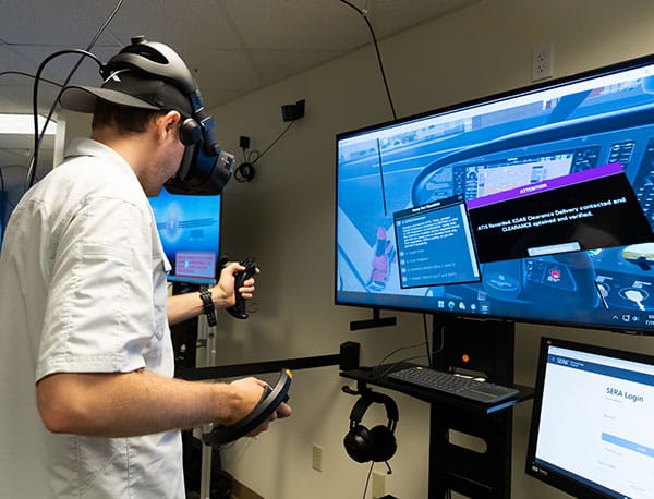 A student uses a virtual reality headset while operating a flight simulator program.