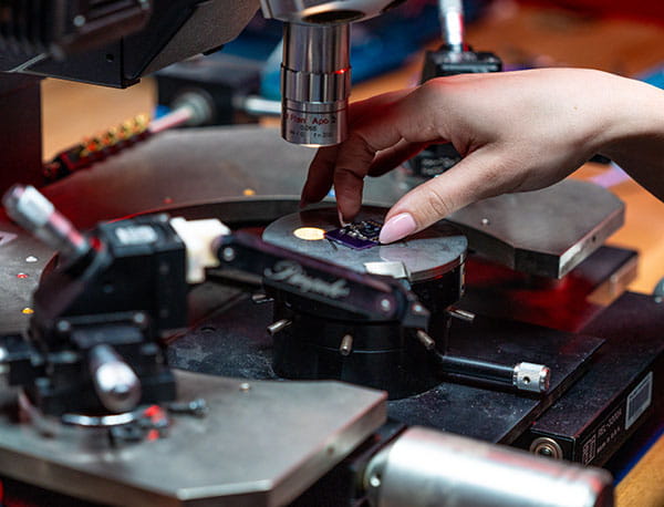 A female Embry-Riddle student adjusts a small electronic board under a microscope.