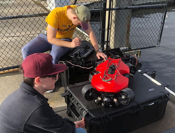 Two students work on a red submarine system.