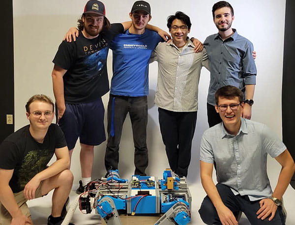 Six students pose around a robotic device.