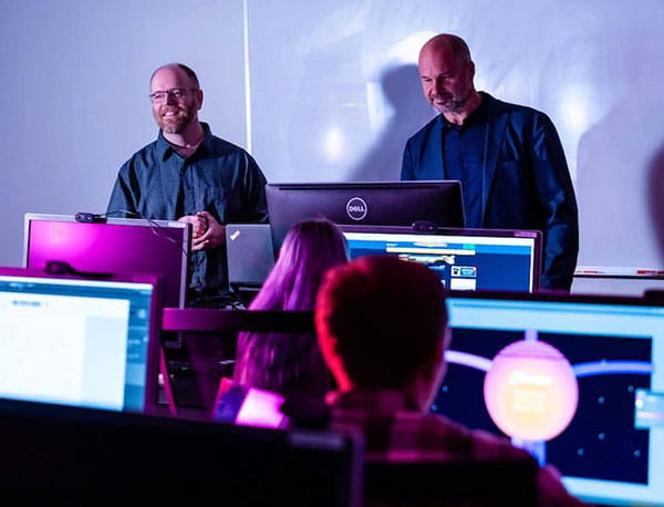 Professors preside over students in a classrom lab working at computers.