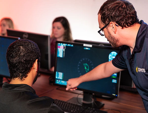 A professor points to a computer screen instructing a student.