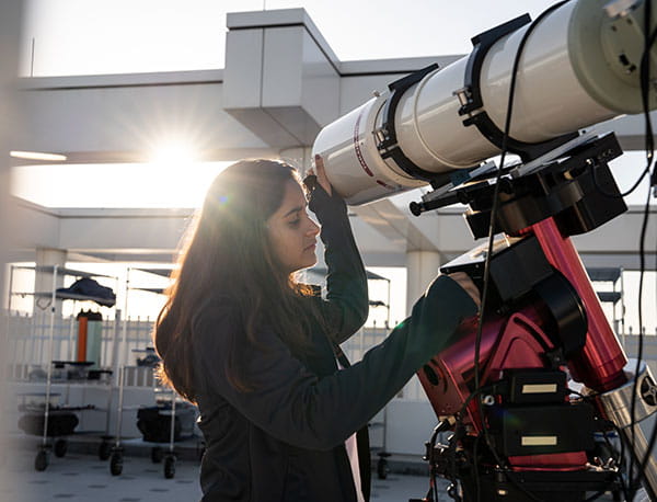A female student works with a telescope while the sun shine into the lab.