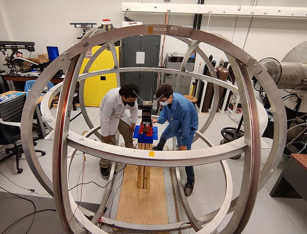 A professor and student work on a device inside a spherical, metal aparatus.