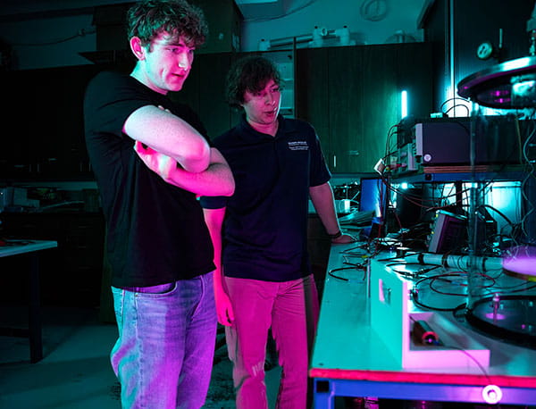 Two people gather over a desk tinted in cyan and pink hues.