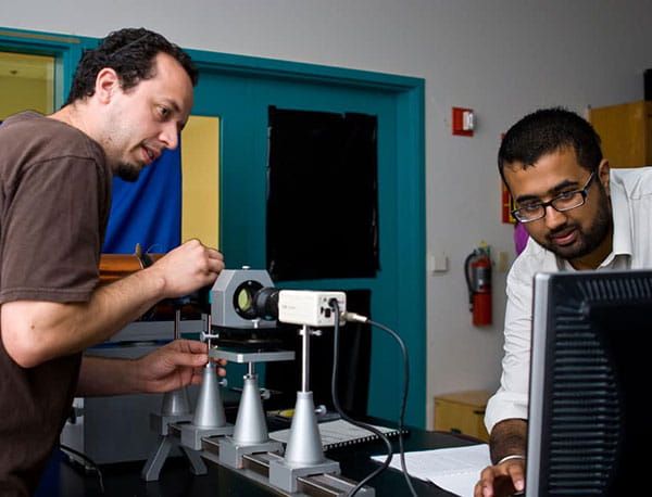 A student and a professor look at a computer screen while working wih a small receiver.