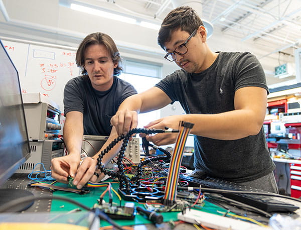 Two people work at a desk putting wires together.