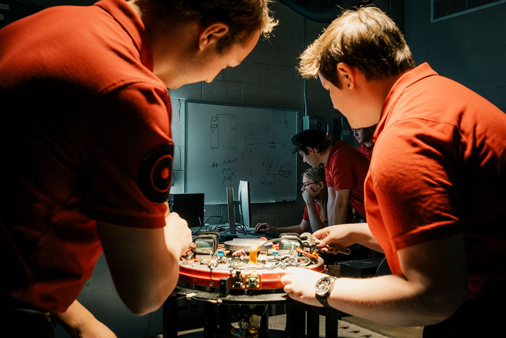 Students work on a lab project in the foreground with students working on a computer in the background