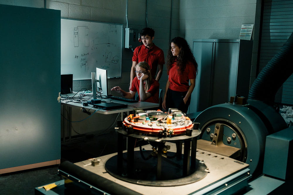 Three Embry-Riddle students look at a computer in the Structural Dynamics Lab