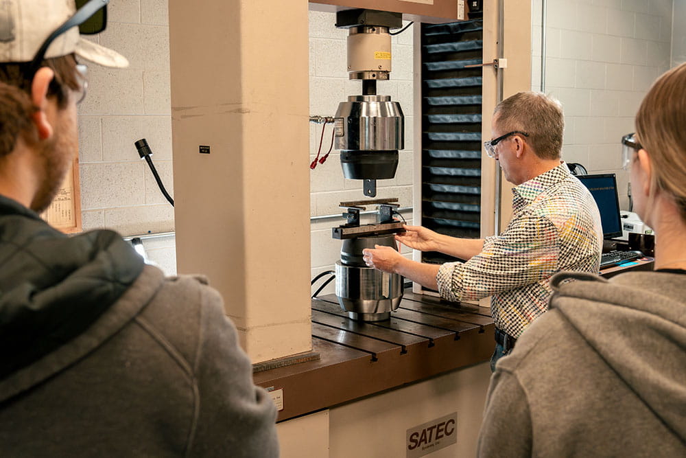 The lab director of the Structural Testing Lab shows students how to use a piece of lab equipment