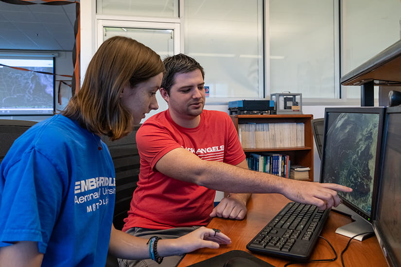 Two Embry-Riddle students sit at a computer looking at weather models