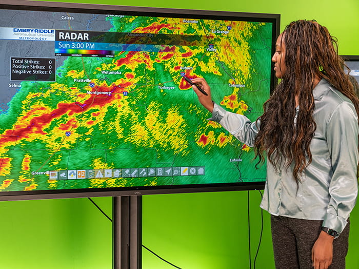 Embry-Riddle student stands in front of a large monitor that shows severe weather on a weather map