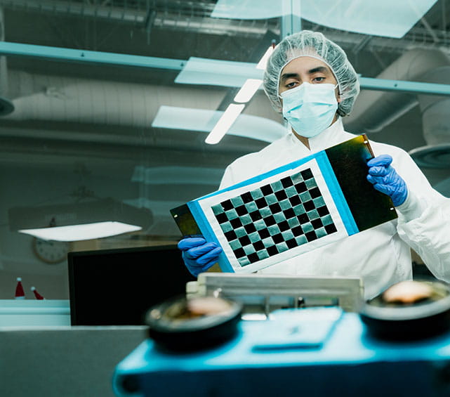 A person in protective gear examining electronic equipment in a laboratory setting