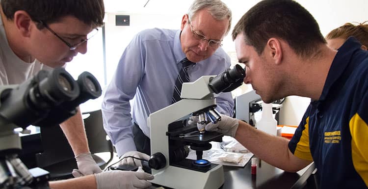 Students look in microscope with professor