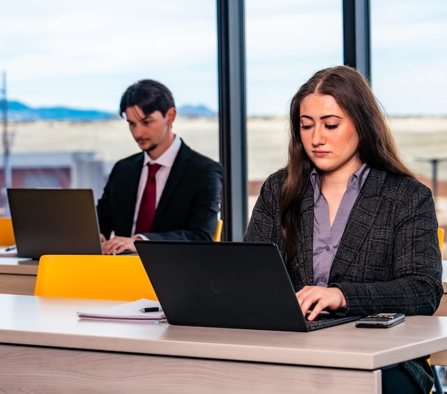 Embry-Riddle students in professional dress sit at tables working on laptops