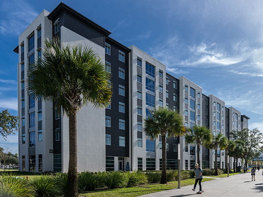 Exterior image of Residence Hall 3 with students walking on a palm tree-lined sidewalk