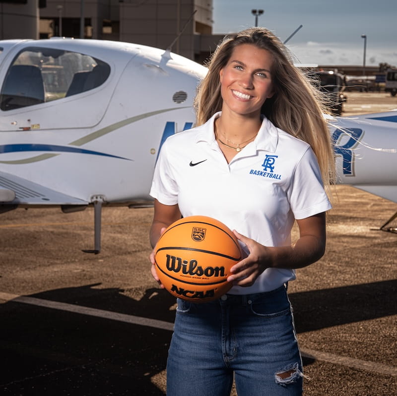 Embry-Riddle graduate, Mary Lengemann, stands in front of a plane on the tarmac holding a basketball