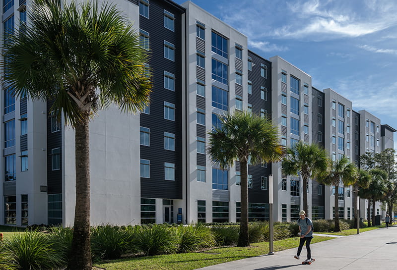 Exterior image of Residence Hall 3 with students walking on a palm tree-lined sidewalk