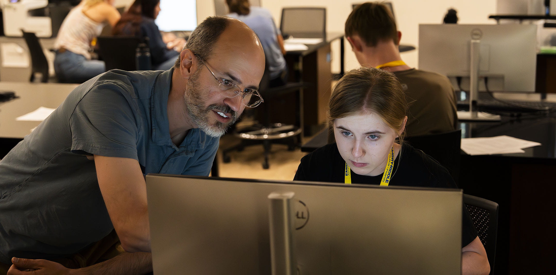 A man works with a student on a computer in a lab on campus