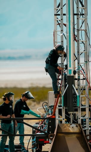 Students assemble and wire a vertical launch rail and sounding rocket on a mobile ground support platform at a desert test site.