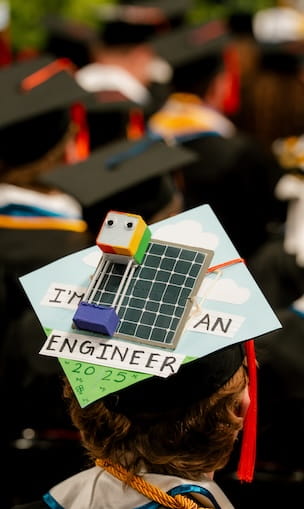 Graduation cap decorated with a three-dimensional model of a solar panel array and the words I’m an Engineer 2025, worn during a commencement ceremony.