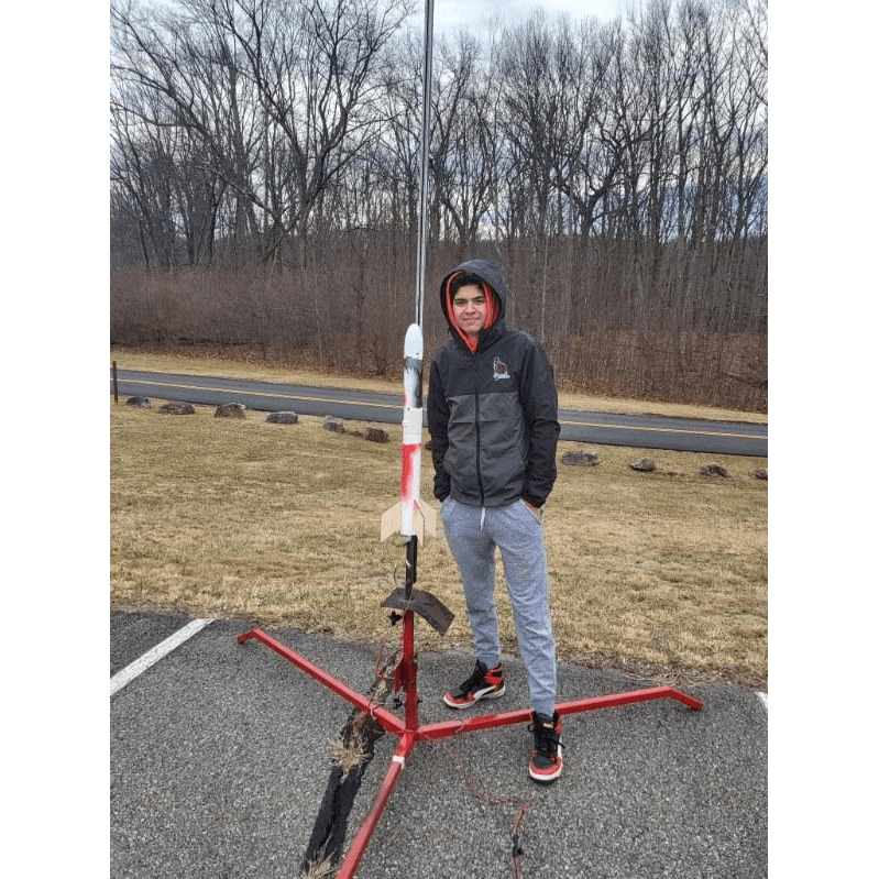 Adam, bundled up in sweats, poses next to a rocket model in a parking lot.